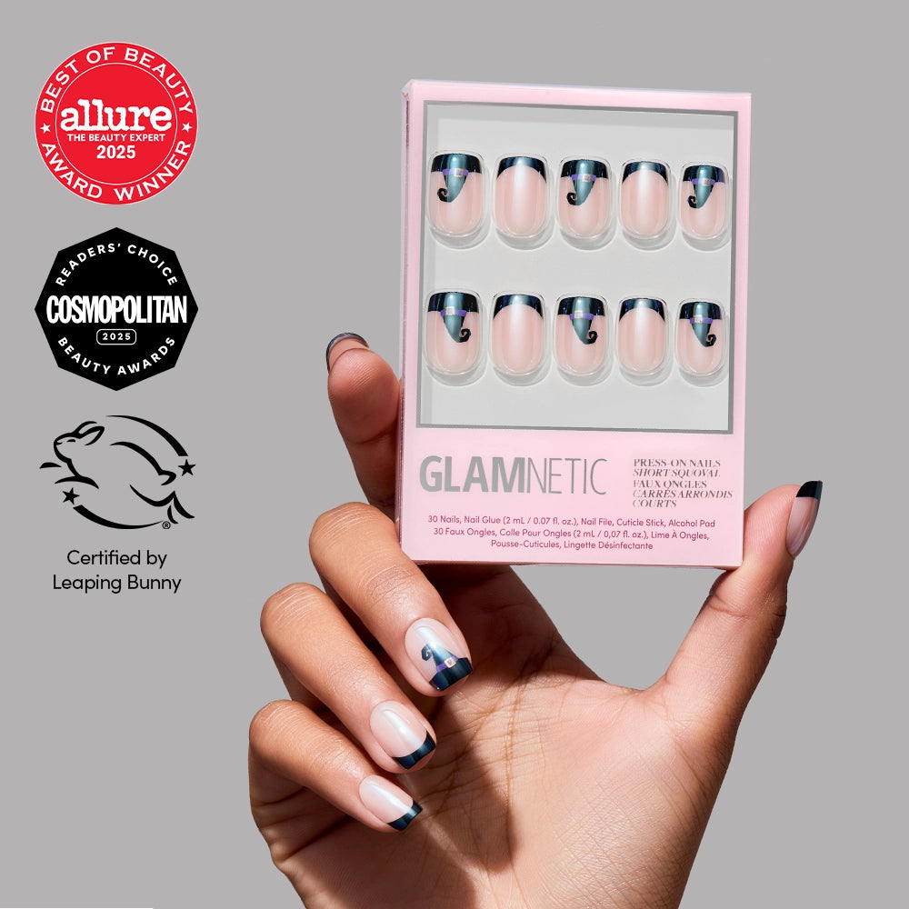 A hand adorned with Glamnetic’s Witchy Woman press-on nails in black and pink French tips holds a Glamnetic nail kit. Set against a gray background decorated with beauty award badges and a cruelty-free certification logo, the short squoval nails add a stylish flair to this striking Witchy Woman Press-On Nails display. - Product image