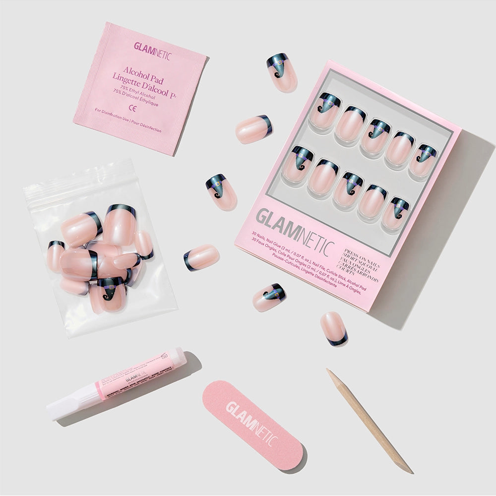 A GLAMNETIC Witchy Woman press-on nail kit in pink, featuring nude short squoval nails with black tips, nail glue, a wooden cuticle stick, nail file, alcohol pad, and an extra bag of nails— all arranged neatly on a light surface. - Product image