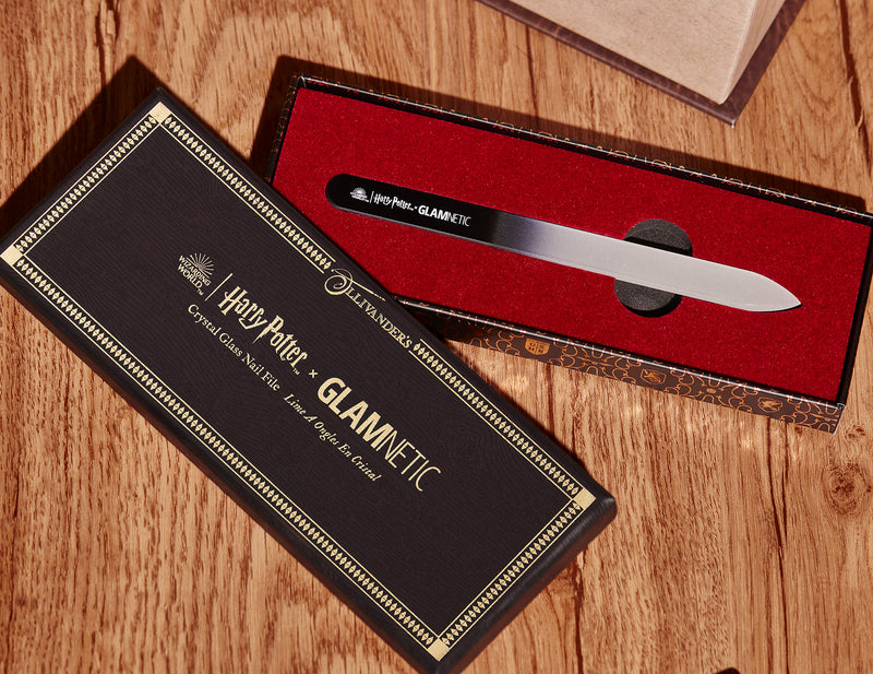 A Harry Potter & Glamnetic nail file in a black and gold box with red velvet lining, displayed on a wooden surface. The file has a black handle with white text and is presented in an open case.