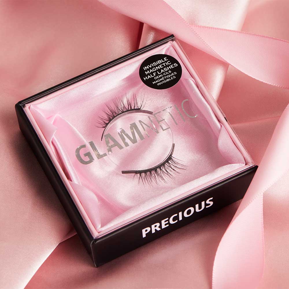 A box of glamnetic Precious magnetic false eyelashes with Cat-Eye Shape and Invisible Magnet Technology is displayed open on pink satin fabric. - Product image