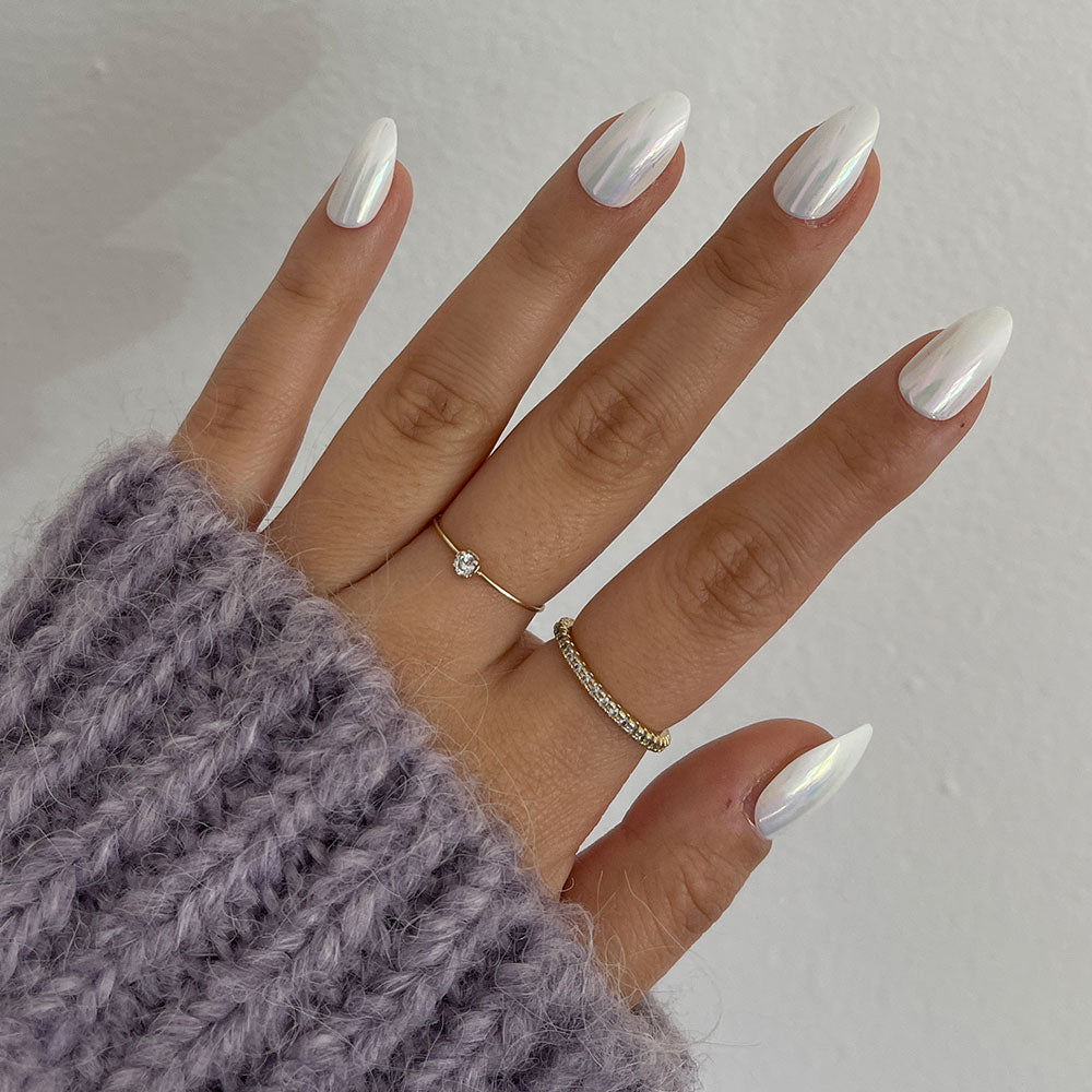 A hand with damage-proof, pearlescent white glamnetic Moonlight nails wears two gold rings. The person sports a chunky lavender knit sweater against a plain white wall background. - Product image