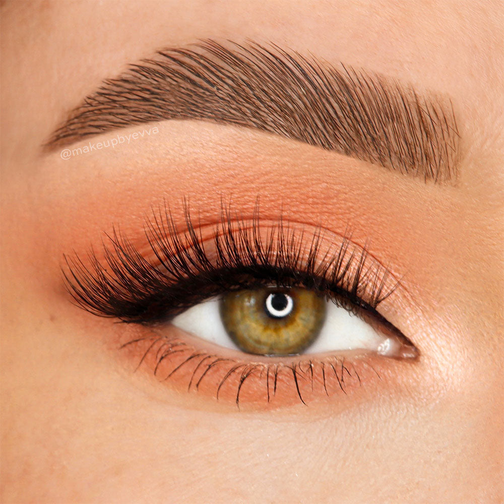 Close-up of a hazel eye wearing glamnetic’s Venus vegan-friendly lashes in a subtle wing, with a groomed brow and peach eyeshadow. Smooth, blended makeup completes this polished look. - Product image