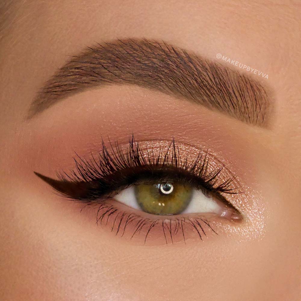 A close-up of a green eye with bold winged black eyeliner, shimmery peach eyeshadow, a well-groomed thick eyebrow, and long vegan Babygirl lash extensions by glamnetic. - Product image